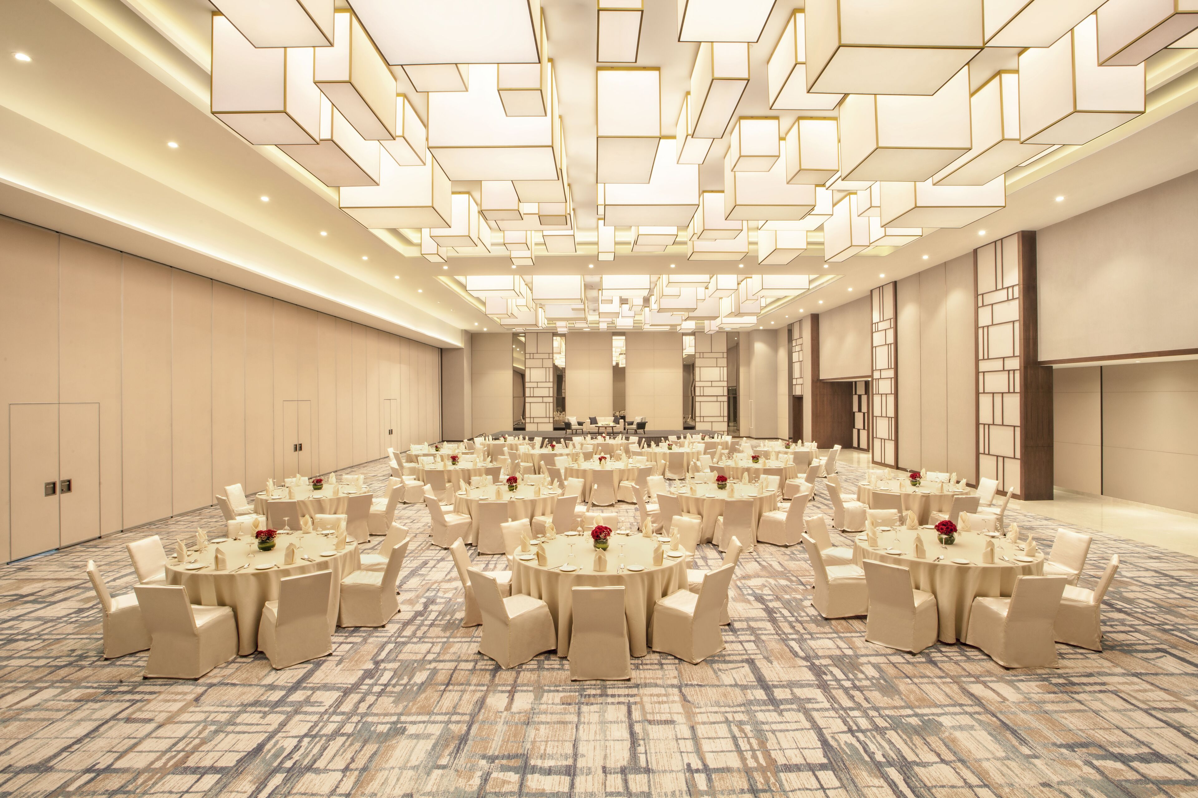 Une grande salle de conférence dotée de plusieurs tables rondes et de chaises, d’un tapis à motifs et d’un design de plafond moderne.