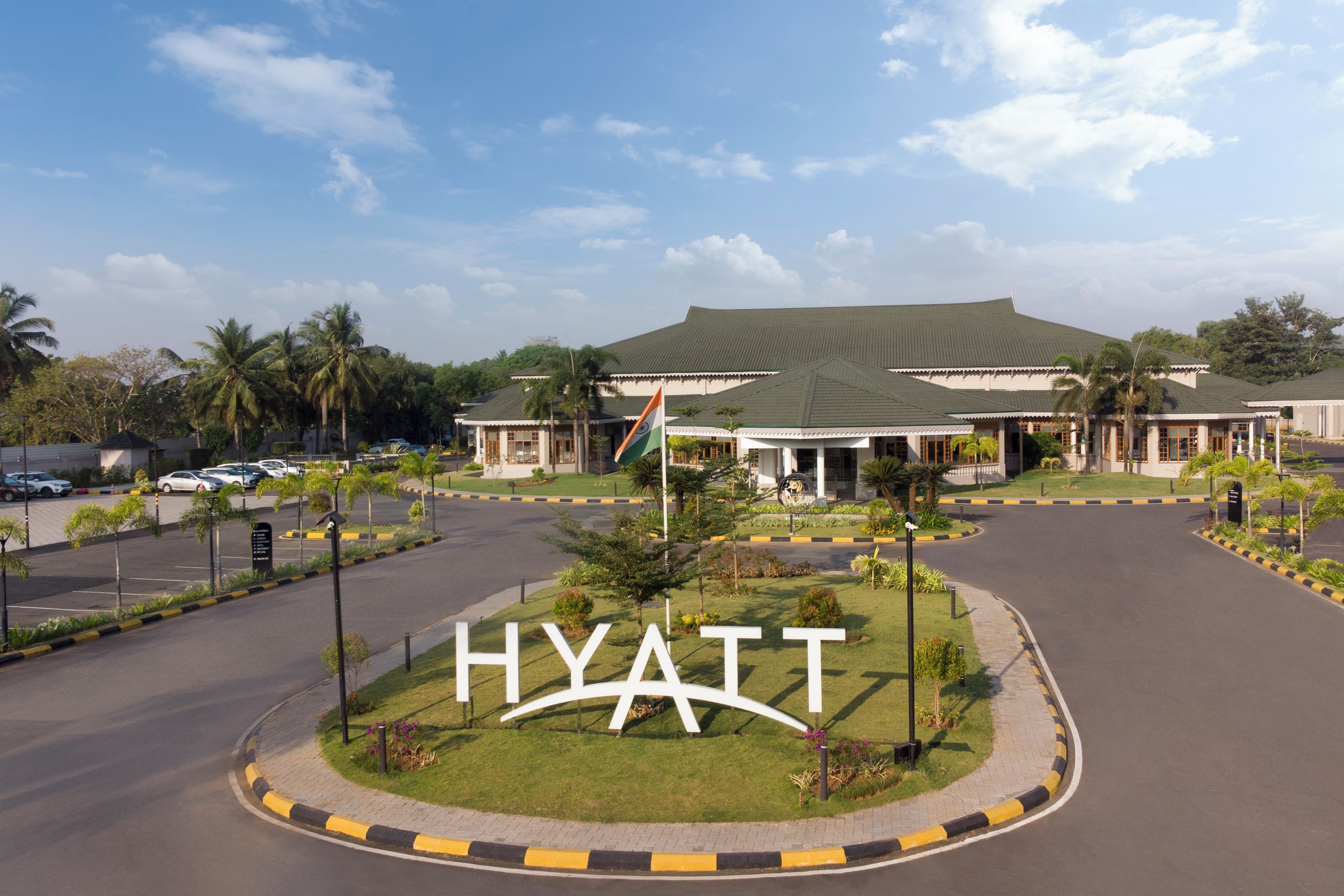 Een hotelingang met een groot 'HYATT' bord, palmbomen en een parkeerplaats.