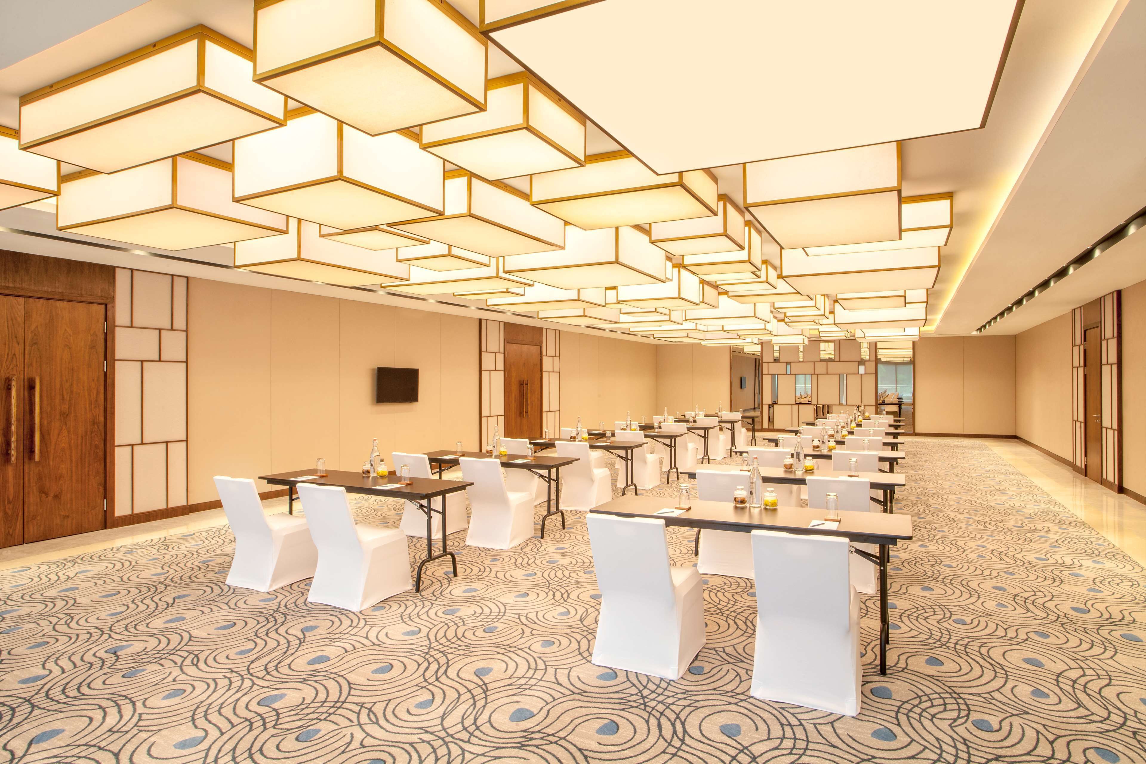 A conference room with tables and chairs, a patterned carpet, and a modern ceiling design.