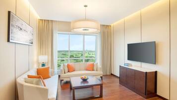 Et moderne hotelværelse med sofa, sofabord, TV og et stort vindue med udsigt over landskabet.