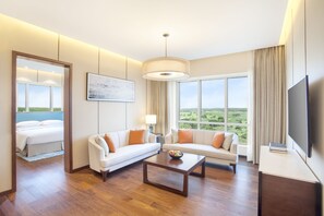 A modern hotel room with a large bed, two sofas, a coffee table, a TV, and a large window with a view of the countryside. - Hyatt Regency Thrissur (Thrissur)