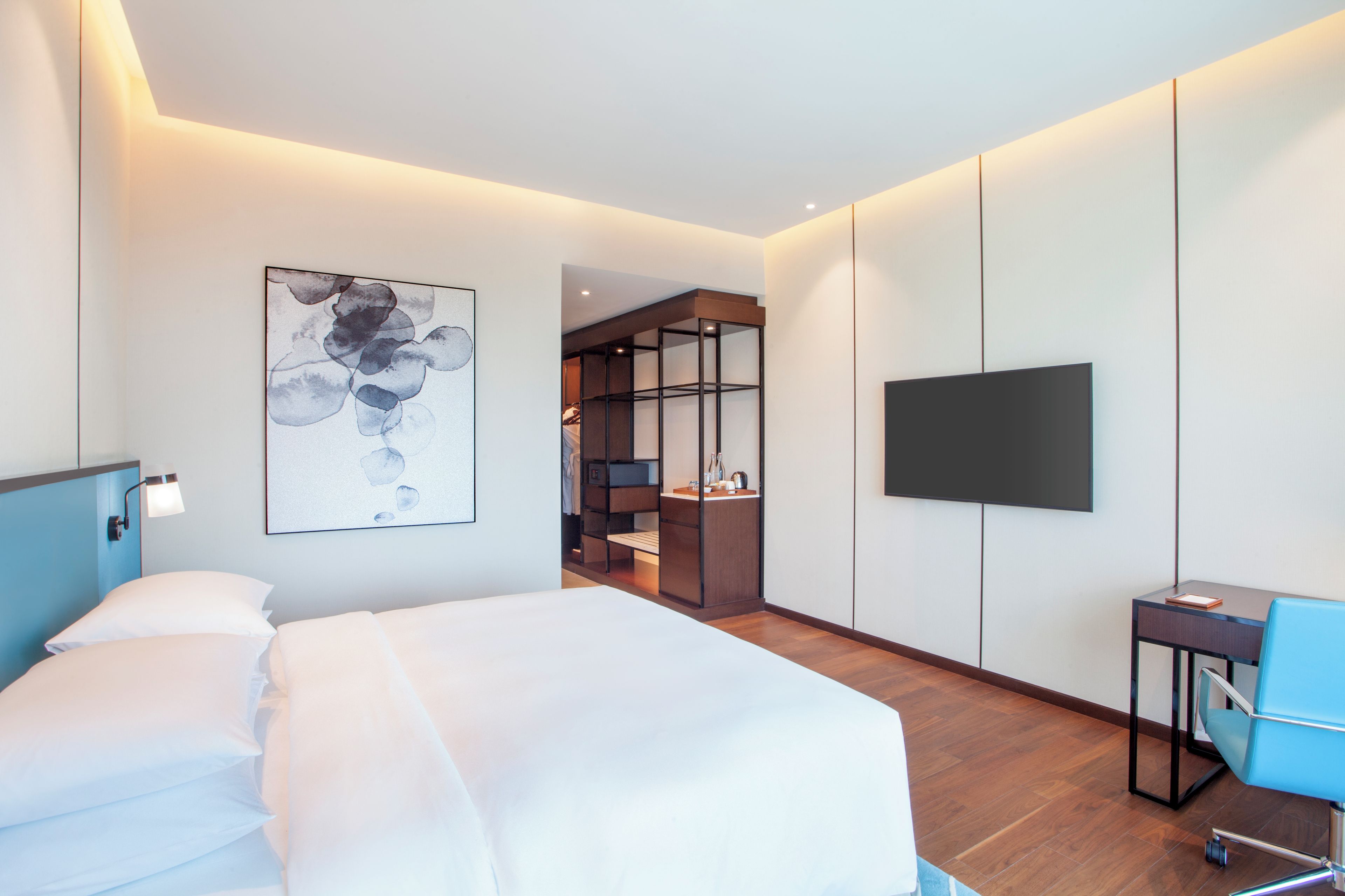 Habitación de hotel con cama, escritorio, silla, televisión y baño visible a través de una puerta abierta.