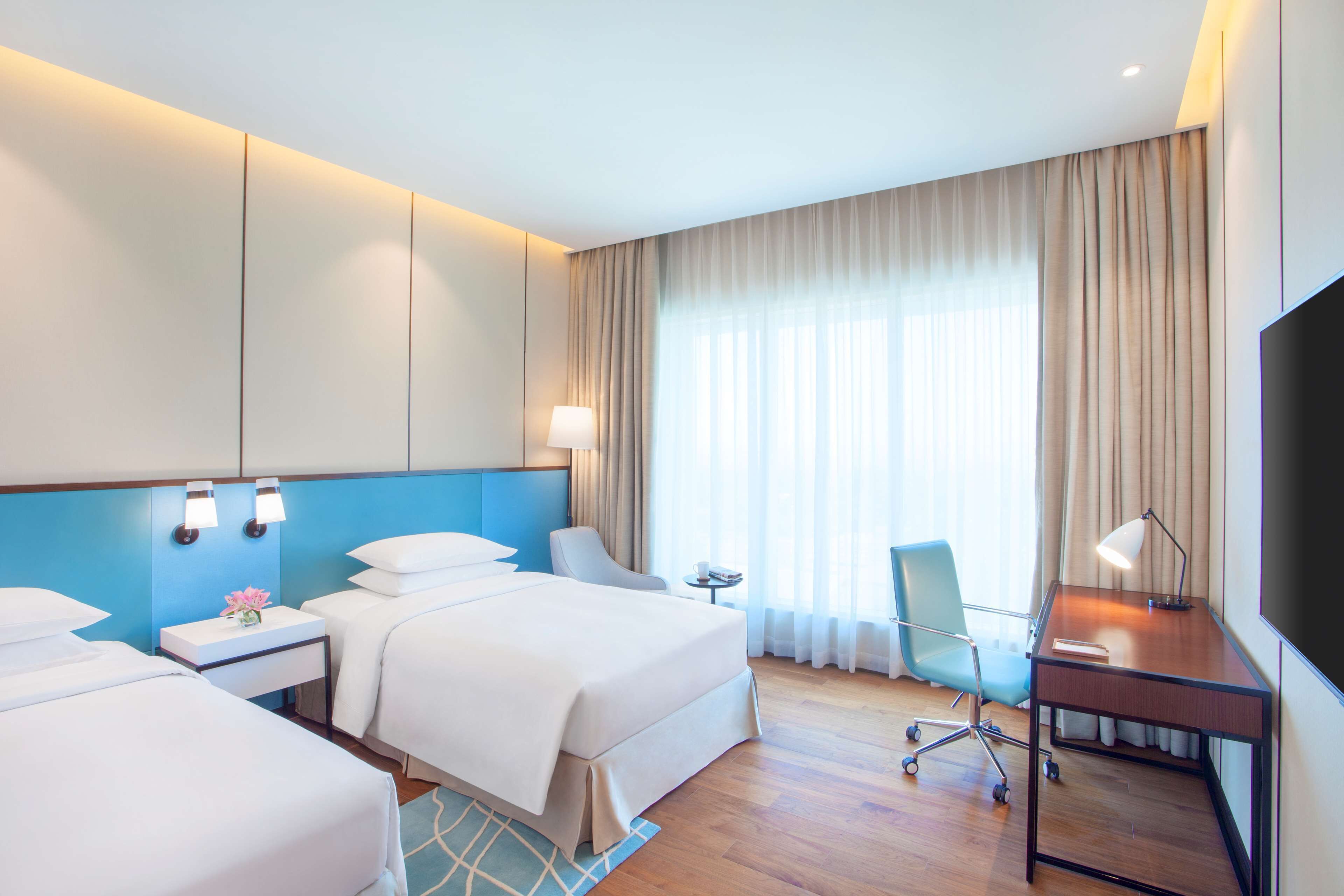 A hotel room with two beds, a desk, a chair, a TV, and a window with curtains.
