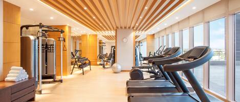 Un gimnasio moderno con cintas de correr, máquinas de ejercicio y un amplio ventanal con vistas a la ciudad.