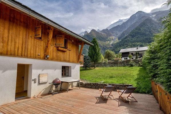 A wooden chalet with a deck, a barbecue, and a view of mountains.