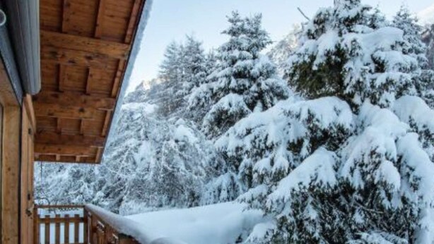Een houten chalet met een overdekte veranda en een sneeuwbedekte pad erheen.