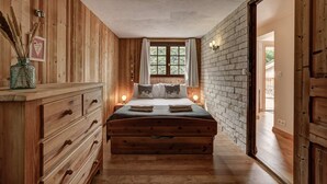Een houten slaapkamer met een bed, nachtlampjes, een kaptafel en een raam met gordijnen.