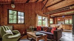Een gezellig cabin interieur met houten wanden, een bank, een groene fauteuil, een salontafel, en een keuken met houten kastjes en hanglampen.