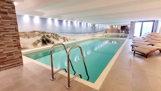 An indoor swimming pool with a beach mural, lounge chairs, and a tiled floor. - Hotel Sylter Blaumuschel (Sylt)