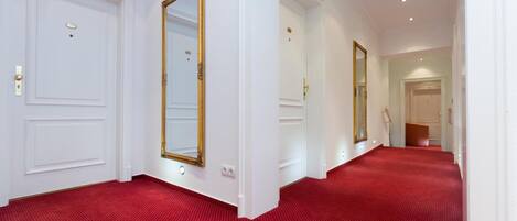 A hallway with red carpet, white walls, and gold-framed mirrors.