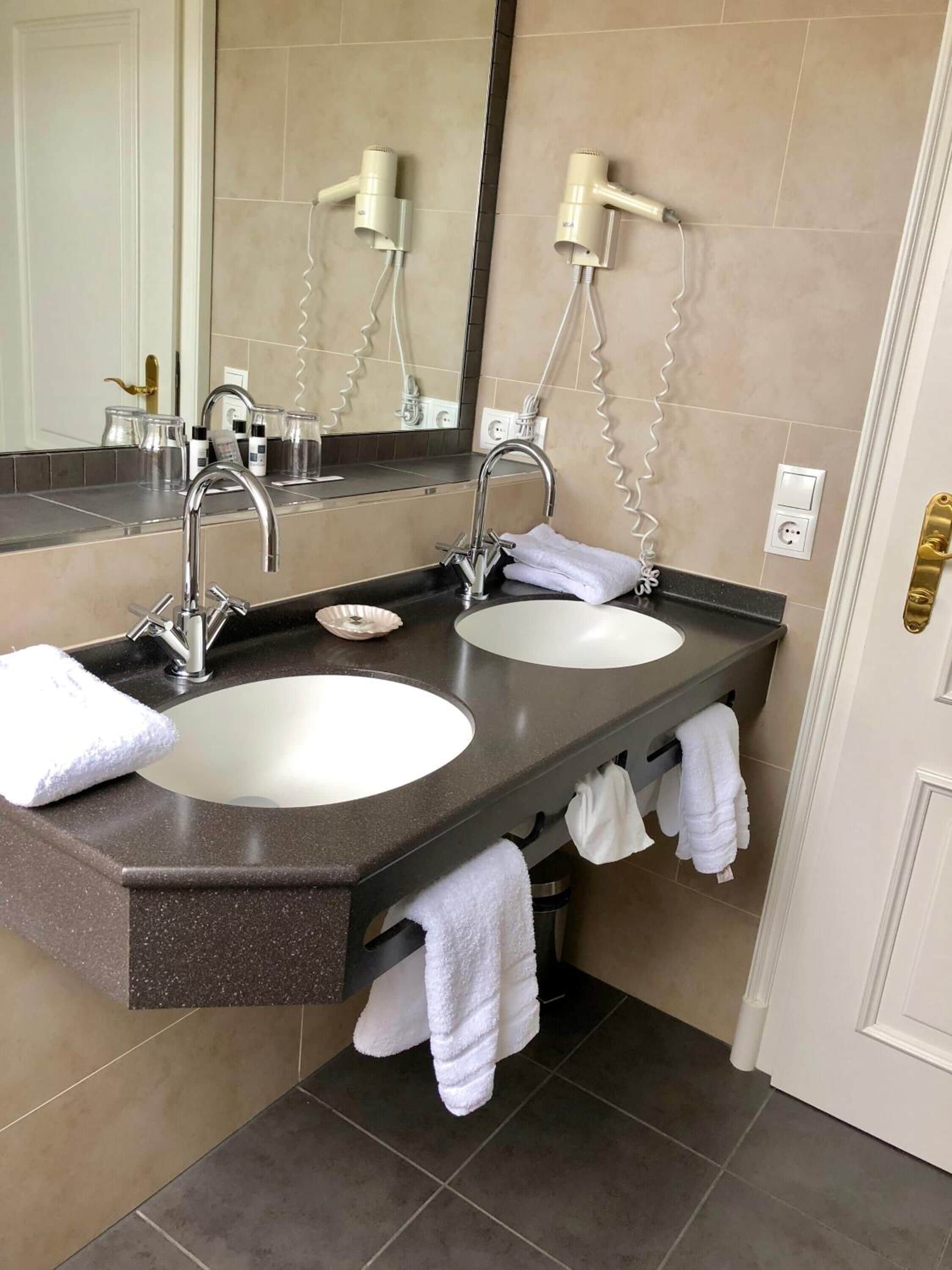 Une salle de bain avec deux lavabos, un grand miroir et un sèche-cheveux fixé au mur.