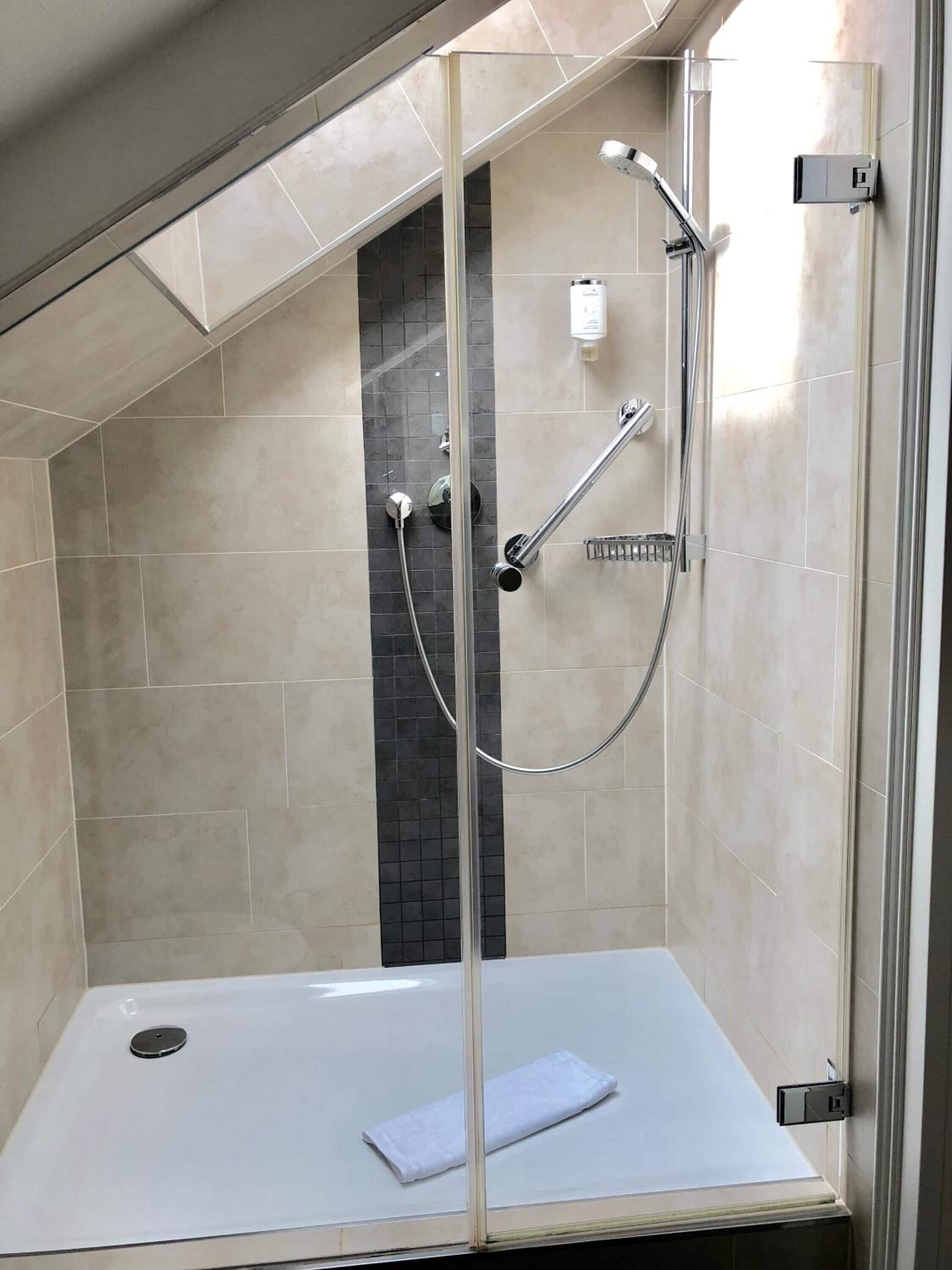 A modern shower enclosure with a glass door, a white sink, and a towel on the floor.