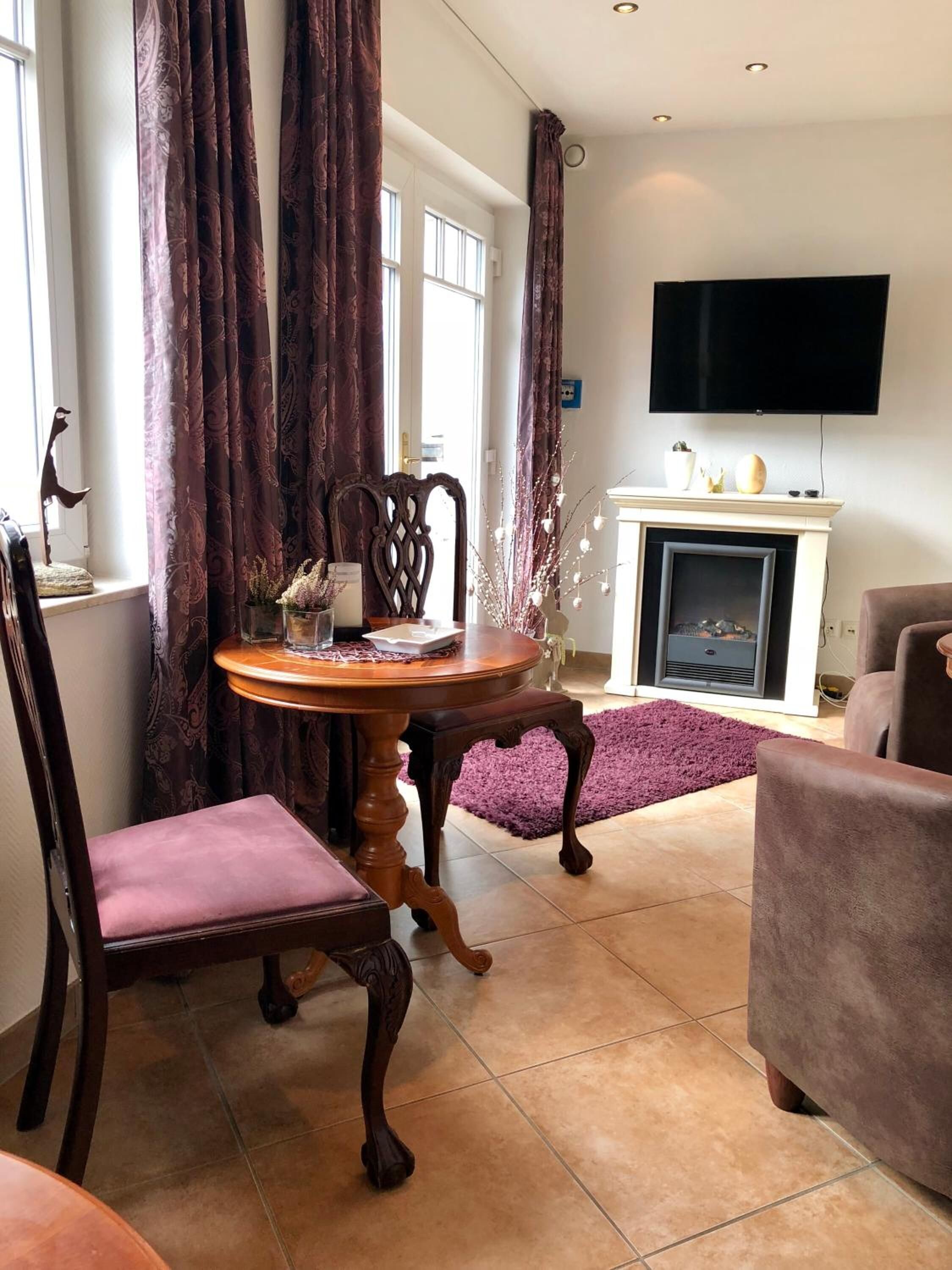 A living room with a fireplace, a television mounted on the wall, and a dining table with chairs.