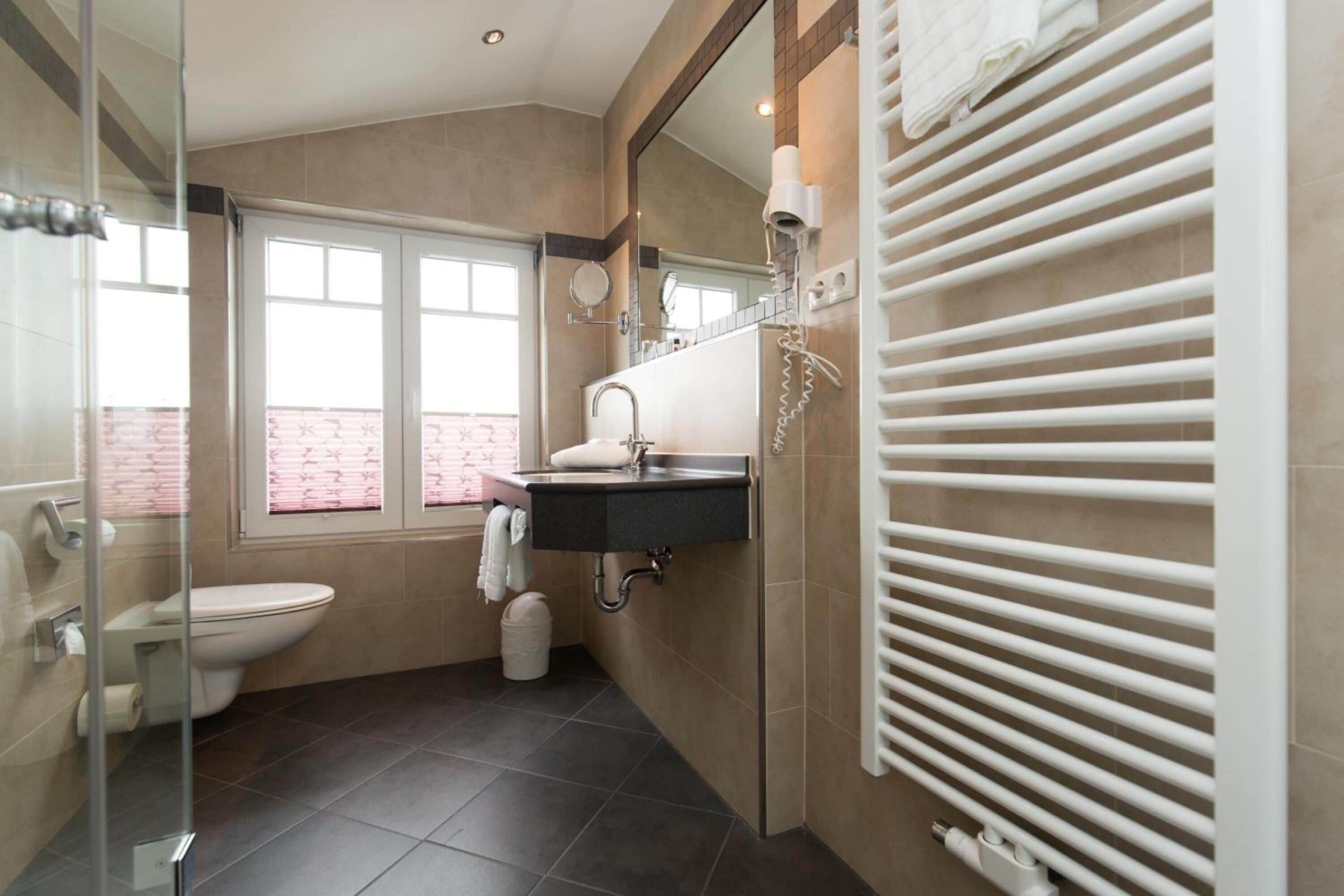 Une salle de bain moderne avec une douche à parois de verre, des toilettes blanches, un lavabo noir avec un miroir et un porte-serviettes.