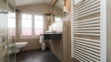 Un baño moderno con cabina de ducha de vidrio, inodoro blanco, lavabo negro con espejo y un perchero para toallas.