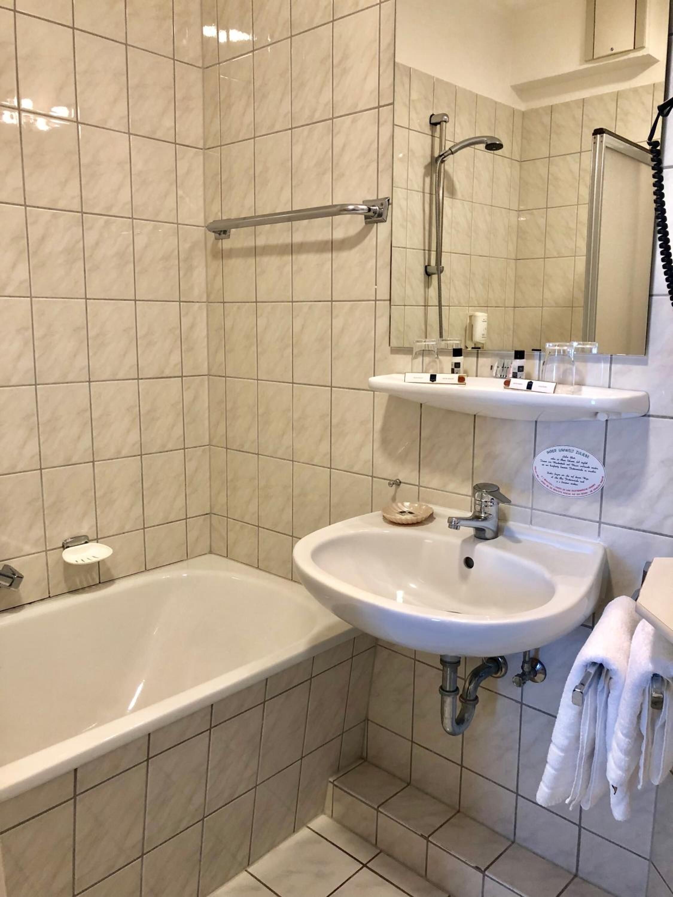 Een badkamer met een bad, wastafel, spiegel en handdoekhouder.