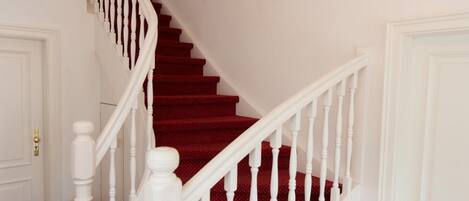 A staircase with white balusters and red carpet, leading to a room with a chandelier.