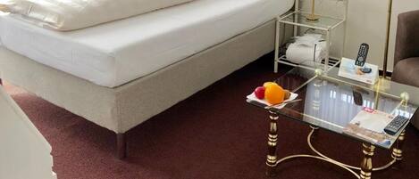 A hotel room with a bed, a glass coffee table with a remote control, a lamp, and a small table with fruits.