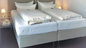 A double bed with white linens, a grey headboard, and a wall-mounted painting of a sunset. - Hotel Sylter Blaumuschel (Sylt)