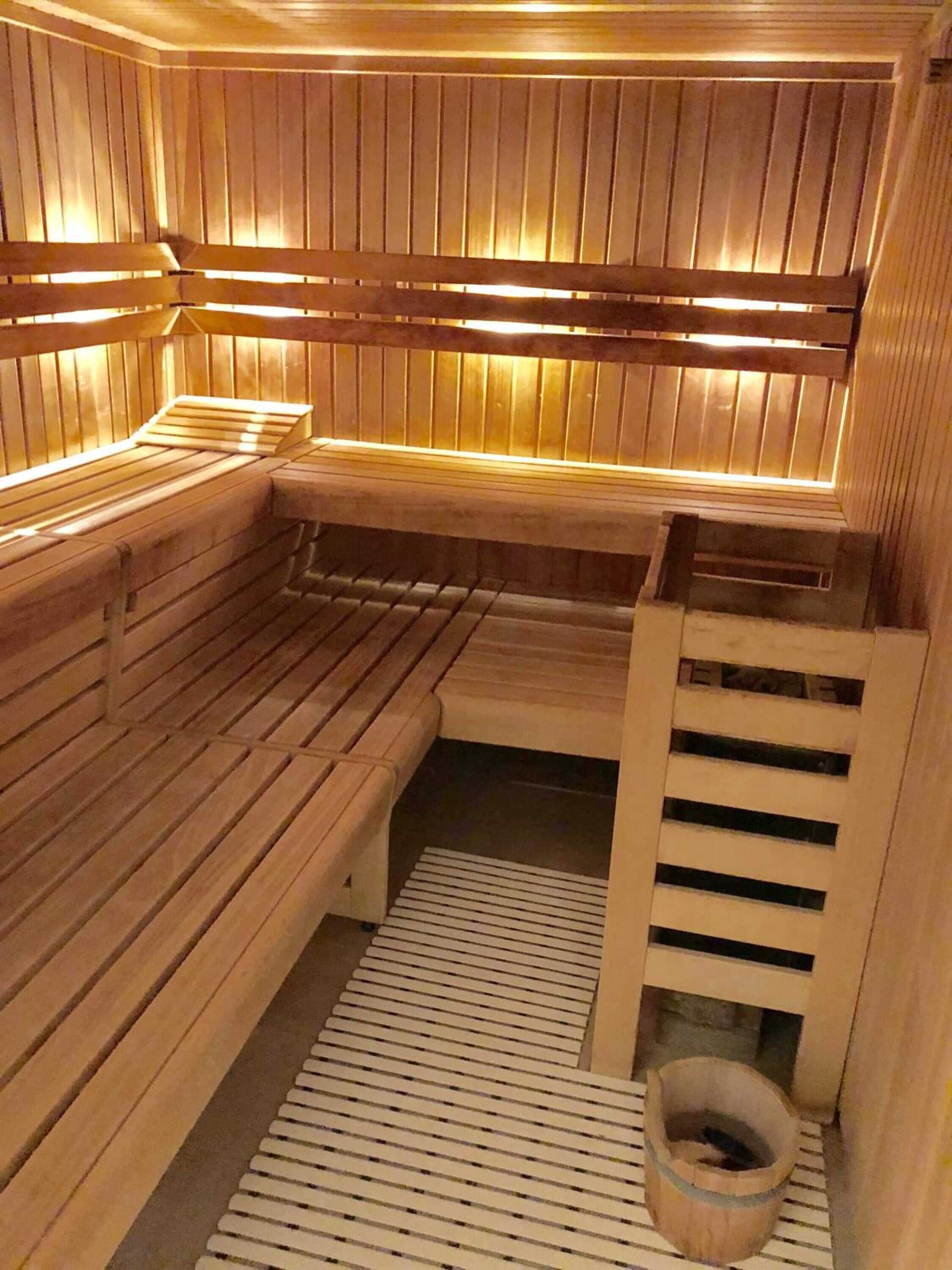 A sauna with wooden benches and benches, a slatted floor, and a wooden bucket.
