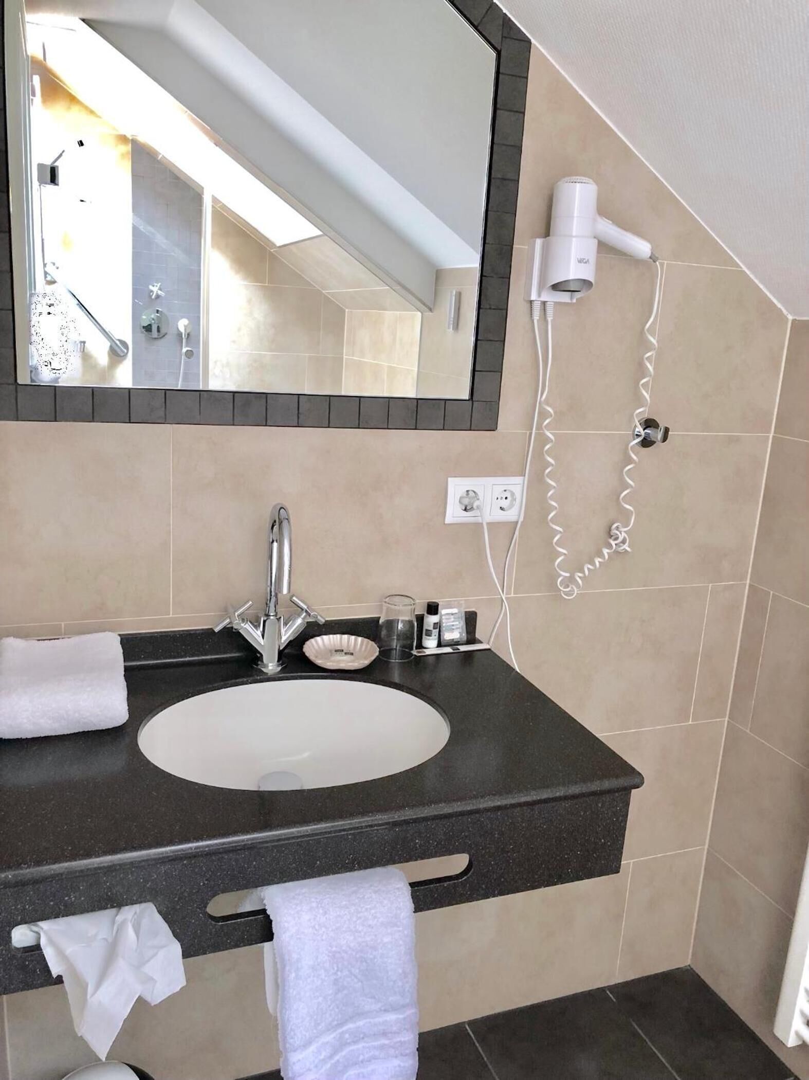 Un baño moderno con un espejo grande, un lavamanos, un perchero para toallas y un secador de pelo montado en la pared.