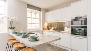 Una cocina moderna con armarios blancos, una isla central con taburetes y un horno.