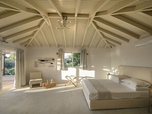 A bedroom with a large bed, a desk, and a chair. There is a window with curtains, a ceiling fan, and a view of greenery outside. - Ilya Suites in Alonnisos, Sporades Islands, Greek Islands, (Steni Vala)