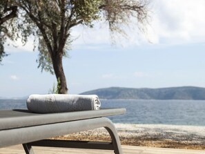 A lounge chair with a towel, overlooking a body of water and distant hills. - Ilya Suites in Alonnisos, Sporades Islands, Greek Islands, (Steni Vala)