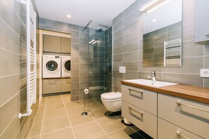 A modern bathroom with a shower, toilet, sink, and a laundry area.