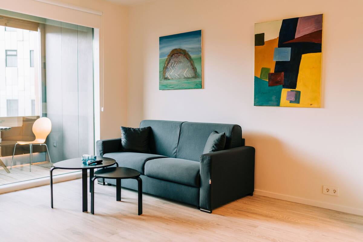 A modern living room with a grey sofa, a small round table, and a painting on the wall.
