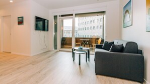 A modern living room with a grey sofa, a small round table, and a flat-screen TV mounted on the wall. - Tower Apartments (Reykjavik)