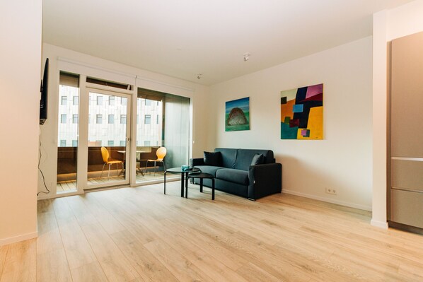 A modern living room with a black sofa, a small coffee table, and a painting on the wall.