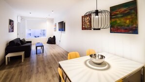 A modern living room with a sofa, a dining table with chairs, a bench, and a large window. - Tower Apartments (Reykjavik)