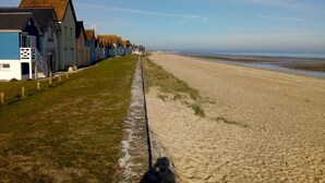 A coastal walkway lined with traditional blue houses with thatched roofs, leading to a sandy beach.