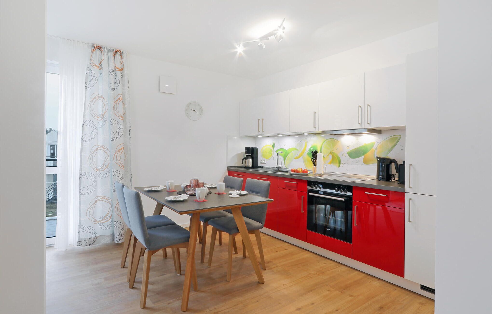 A modern kitchen with red and white cabinetry, a dining table with chairs, and a kitchen island with a coffee maker and fruit.