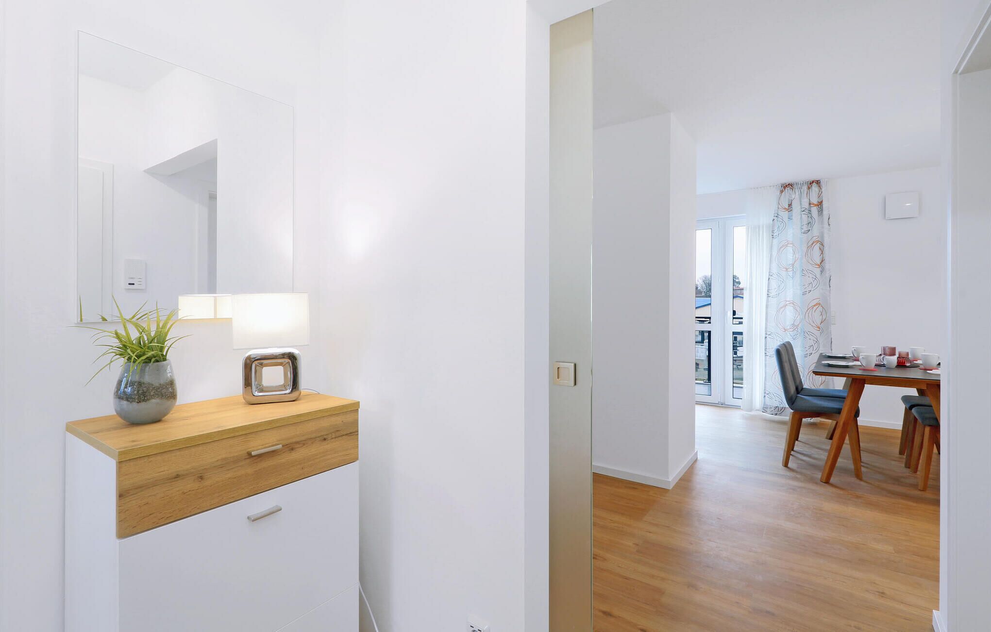 A modern, minimalist bathroom with a wooden vanity, a mirror, a potted plant, and a wall-mounted light.