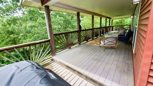 Une véranda couverte avec des balustrades en bois, un coin salon avec un canapé et des fauteuils, et une vue sur une végétation luxuriante.