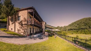 A stone building with a balcony, surrounded by a grassy area and a fence, with a hilly landscape in the background. - Paraíso del Bierzo (Vega de Valcarce)