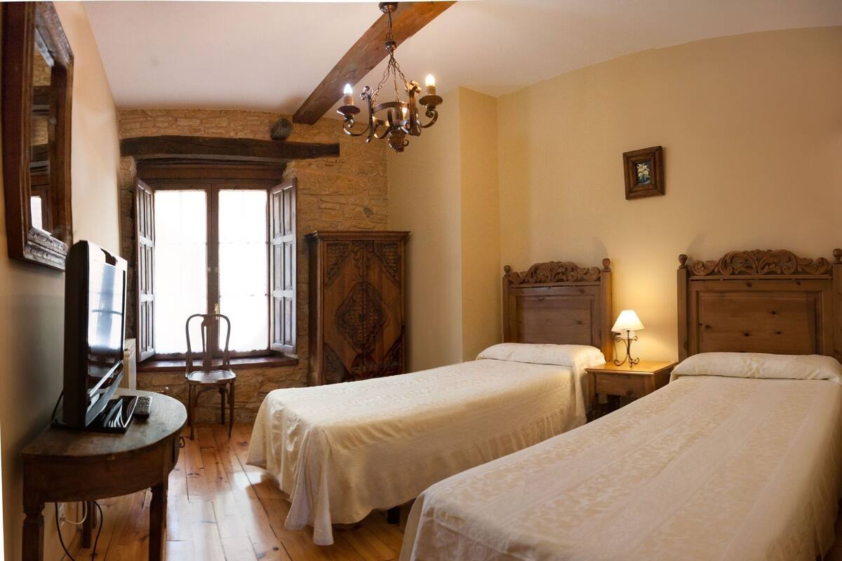 Een kamer met twee bedden, een houten tafel met een afstandsbediening, een stoel en een kroonluchter.