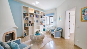 Un salon avec une cheminée, une grande bibliothèque, une table basse en osier et un fauteuil bleu.