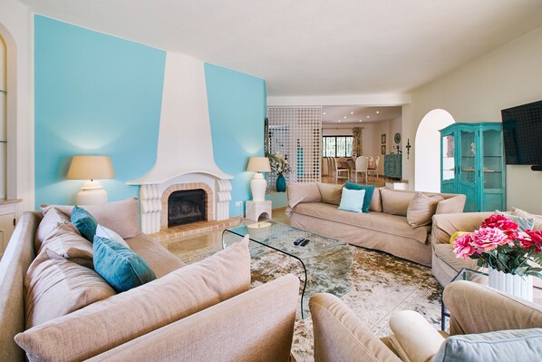A spacious living room with a fireplace, beige sofas, and a glass coffee table. - Villa Shambala (Carvoeiro)