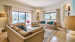 Un salon spacieux avec des canapés de couleur beige, une table basse et une grande fenêtre agrémentée de rideaux.