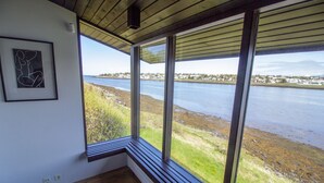 Una habitación con ventanas amplias que dan a una masa de agua y un pueblo lejano.