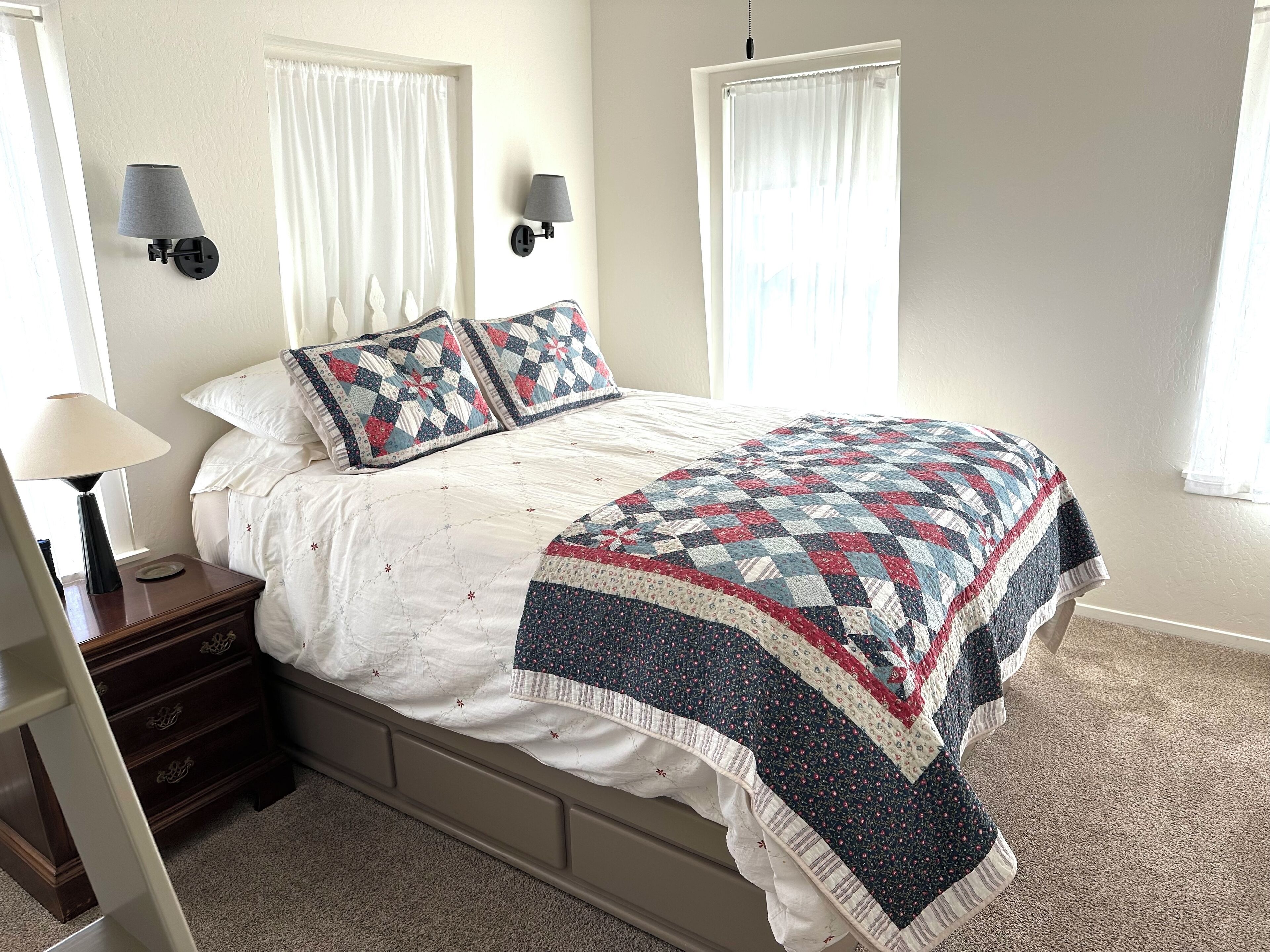 A neatly made bed with a quilt, two wall-mounted lamps, and a nightstand with a lamp.