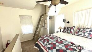 Une chambre à coucher avec un lit, un ventilateur de plafond, une fenêtre avec des rideaux, une échelle et une lampe de chevet.