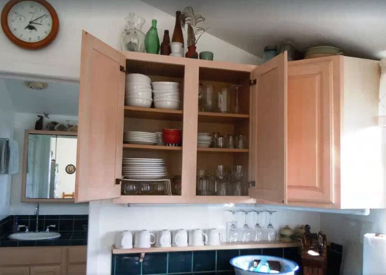 A kitchen with open cabinets containing dishes, glasses, and a sink with a mirror above it.