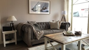 A living room with a grey sofa, a small side table with a lamp, a wooden coffee table, and a framed picture on the wall. - Luxurious apartment for 4 persons with parking directly in front of the terrace (Kühlungsborn-West)