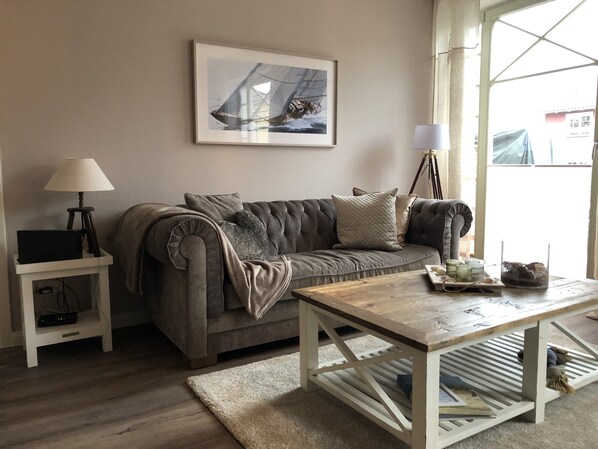 Un salon avec un canapé gris, une petite table d’appoint avec une lampe, une table basse en bois et un tableau encadré au mur.