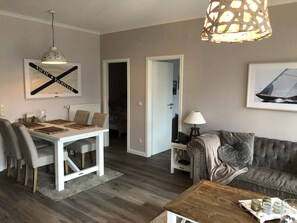 A dining area with a white table and chairs, a wooden coffee table, and a hanging light fixture.