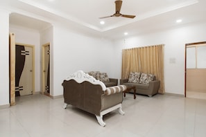 A spacious living room with a ceiling fan, two sofas, and a patterned curtain. - OYO 37499 Saba Service Apartments (Hyderabad)